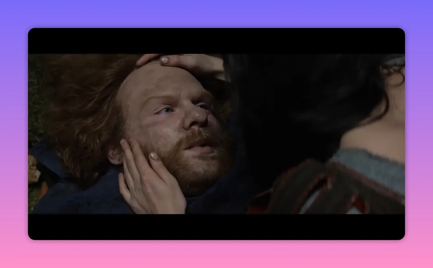 Woman cradling an injured bearded man's head and cheek as she tends him on the ground