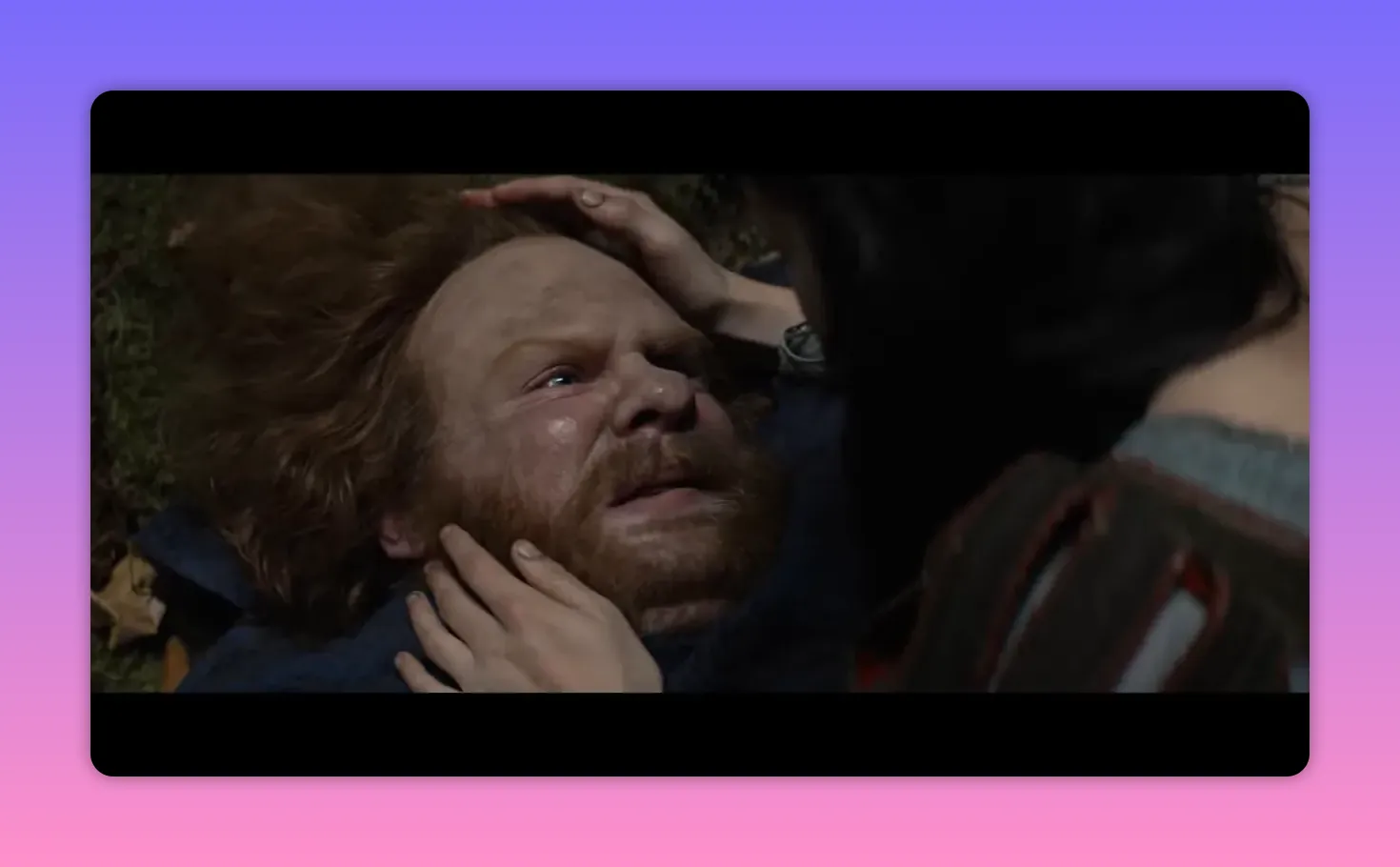 Bearded man lying on the ground being tended by a woman whose hands cradle his head and cheek