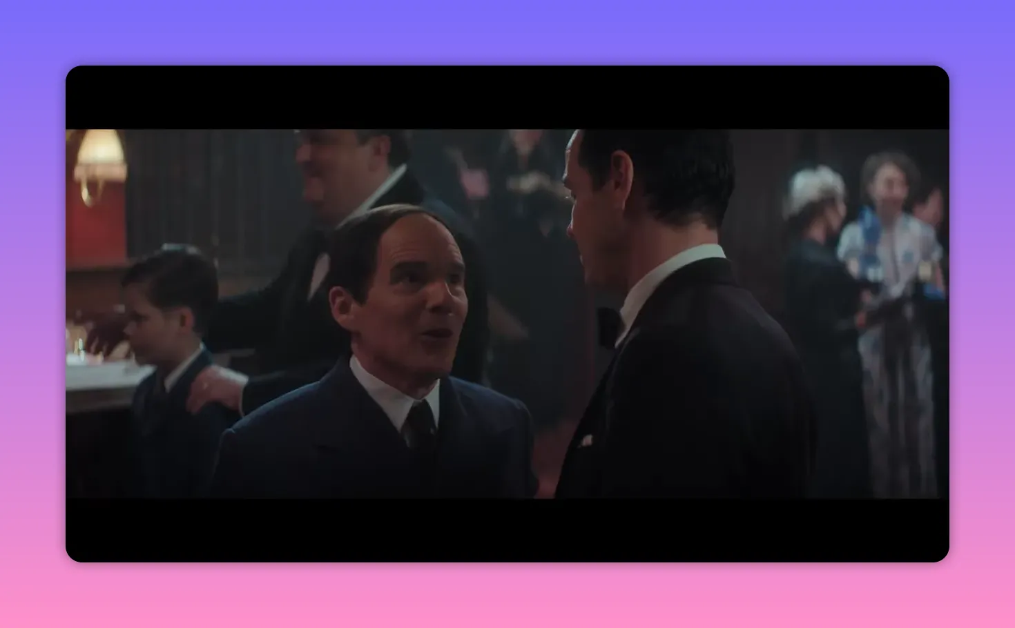 Two men facing each other in a reception; one is speaking animatedly while the other listens