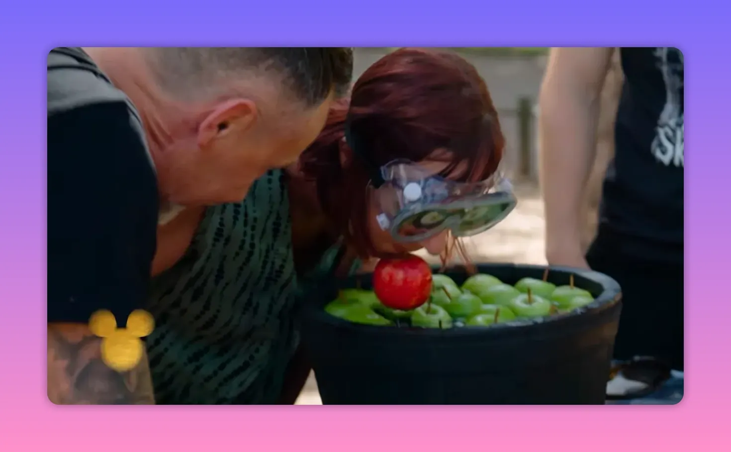 Player wearing goggles lifting a red apple from a tub of green apples with her mouth during the apple-bobbing challenge.