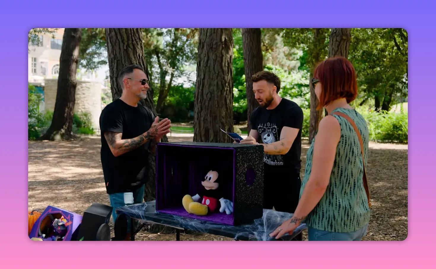 Host explaining the Hands of Horror rules to two contestants while a Mickey Mouse plush sits inside a purple-lined covered box on the table.