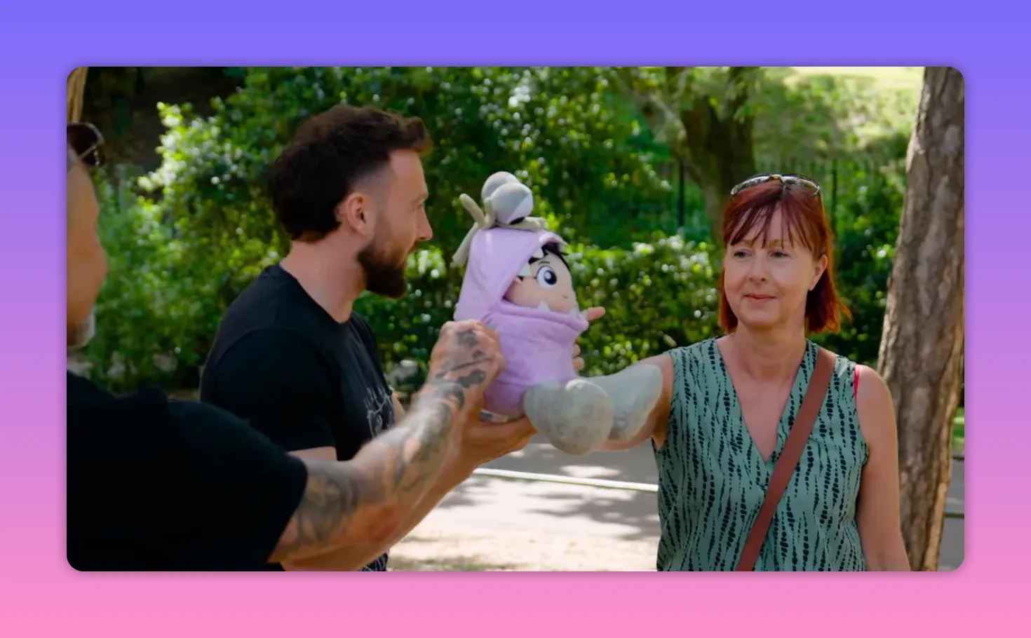 A contestant and the host each holding an arm of a purple Boo doll as the contestant extends her arm, preparing for the final challenge.