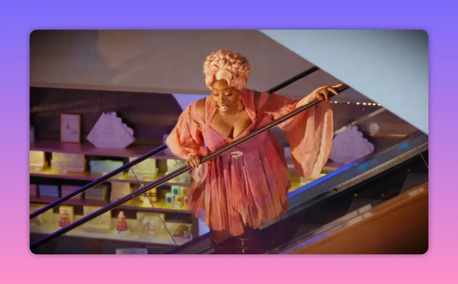 Full-body shot of a performer in a pink theatrical costume descending an escalator at Selfridges during a surprise Disney performance, with store displays visible in the background.