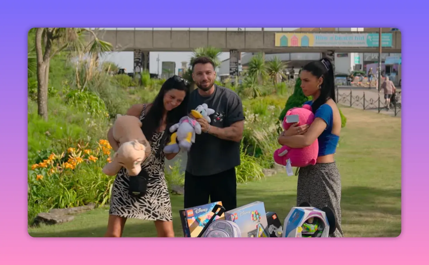 Host and two contestants with oversized plush prizes; one contestant looks amused while another holds a pink plush looking disappointed