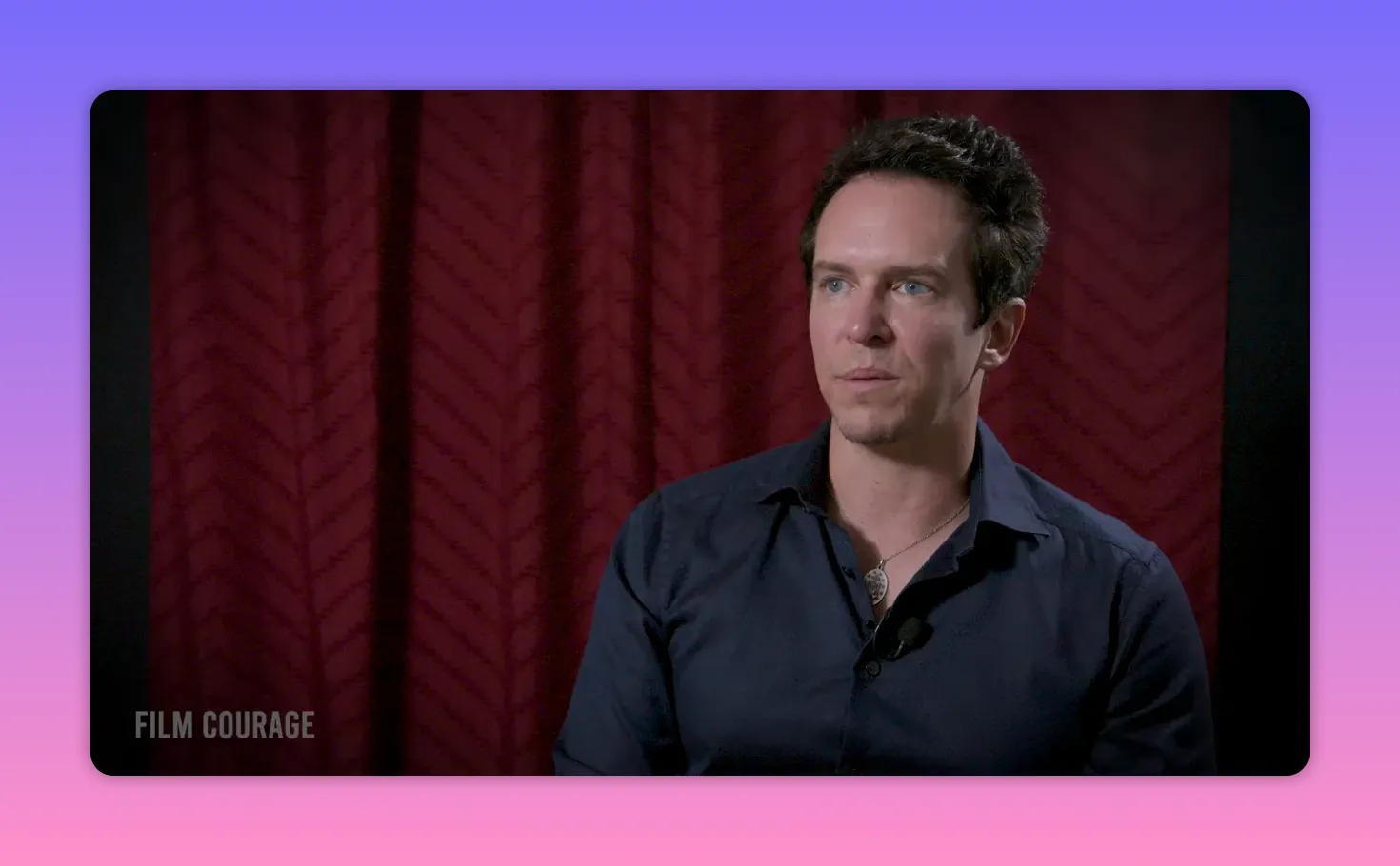 Well-lit interview portrait of a person looking engaged and thoughtful in front of a patterned red curtain.