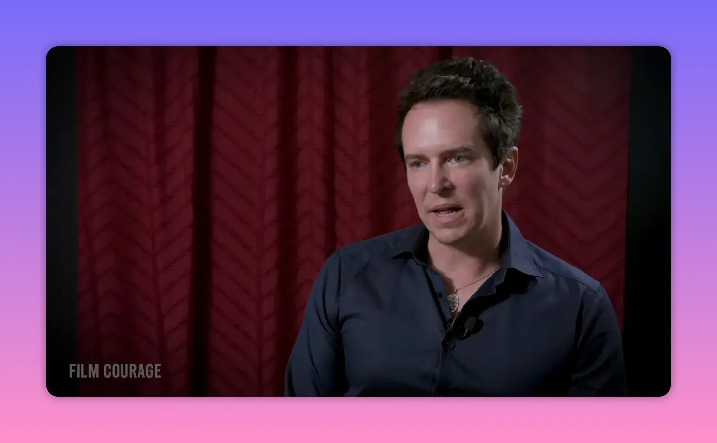 Interviewee speaking directly to camera in front of a red curtain, clear mid-shot with eyes engaged