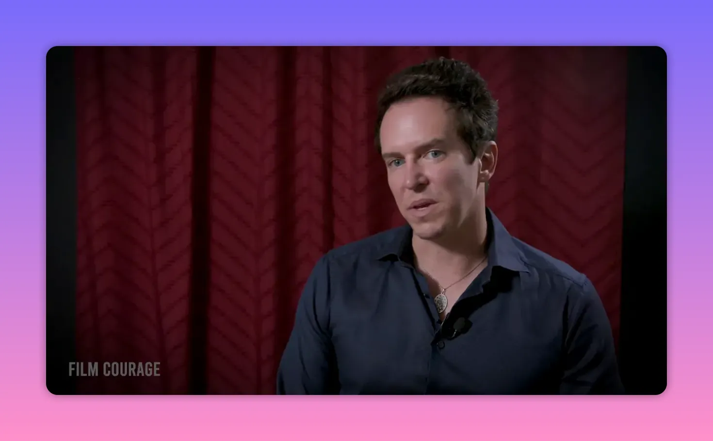 Crisp three-quarter interview shot of a person against a red curtain, showing a lavalier mic and natural lighting.