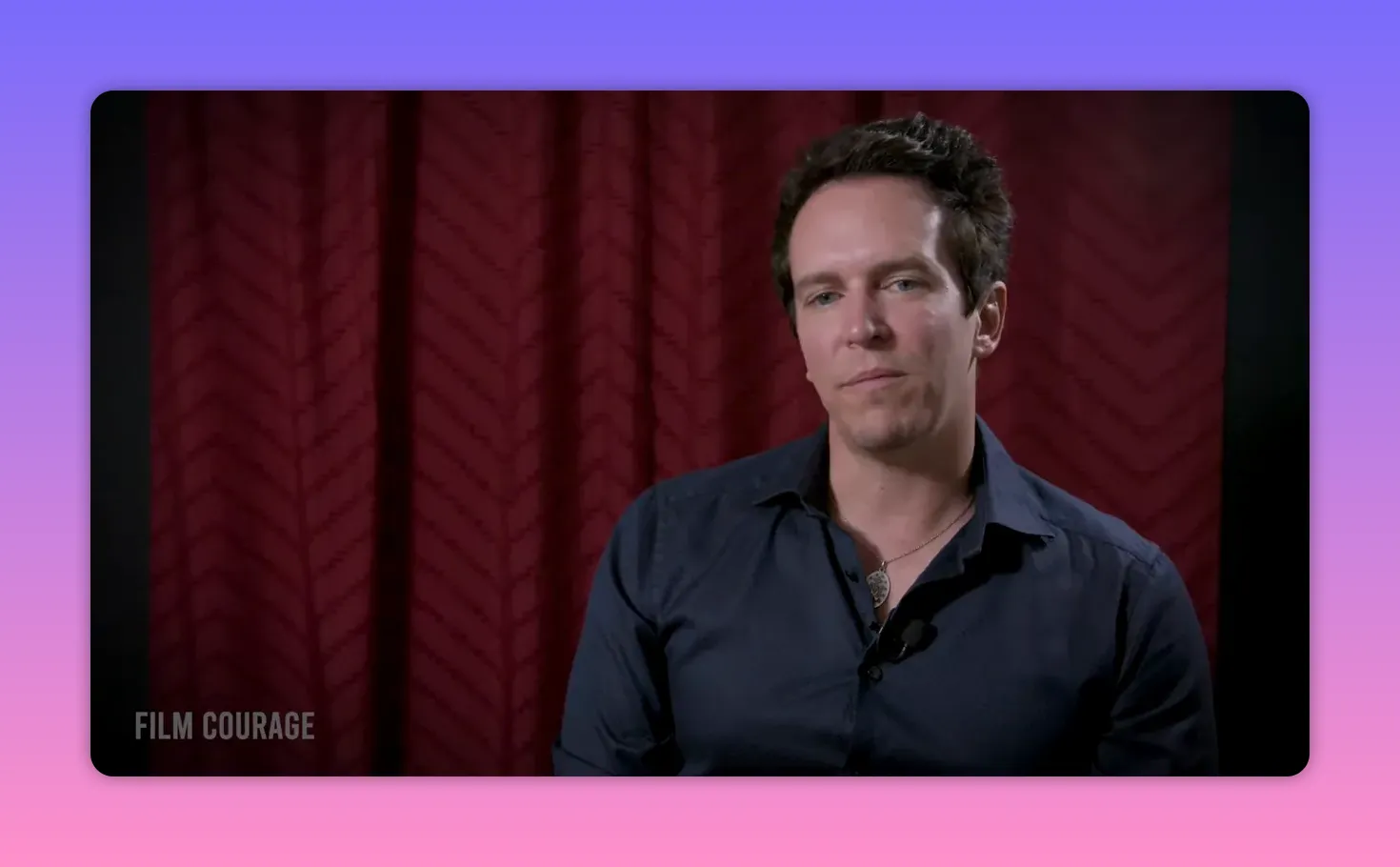 man in interview with contemplative expression against a red curtain backdrop