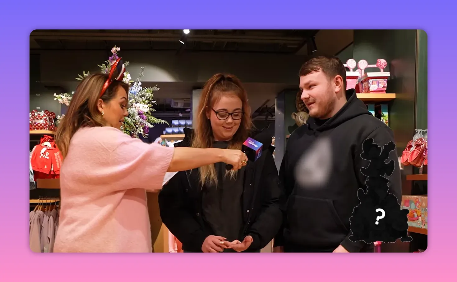 Host extending a microphone to two shoppers in a Disney Store as they prepare to answer trivia