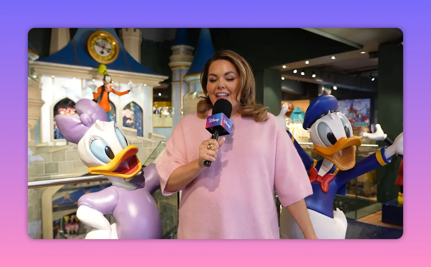 TV presenter holding a microphone between Daisy and Donald statues inside the Disney Store