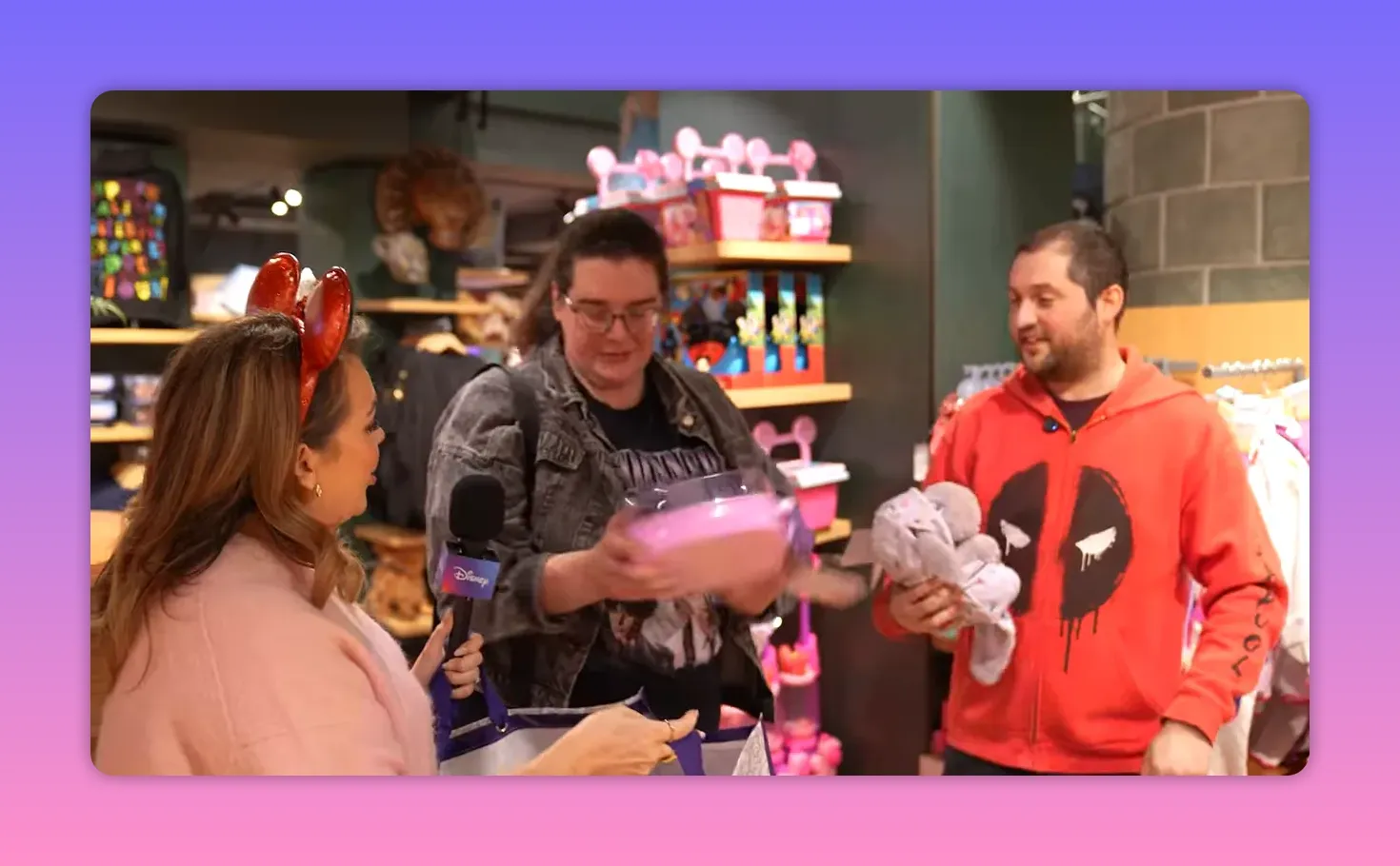 Presenter holding a microphone as two shoppers accept plush toys and a prize bag inside a Disney Store