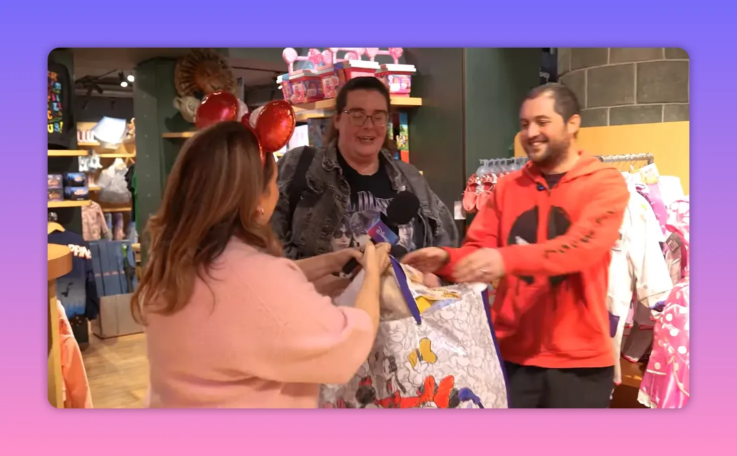 Host handing a large Disney prize bag to two smiling shoppers in the store, celebratory moment