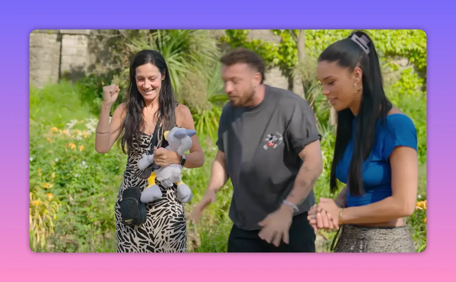 Mother pumping her fist and holding a plush toy while the host and daughter stand beside her smiling in a garden setting.