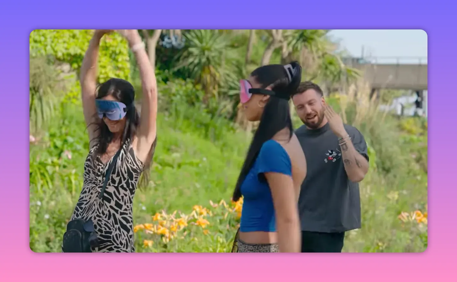 Two blindfolded contestants and the host in a sunny garden; one contestant pumps their arms overhead in a celebratory gesture.