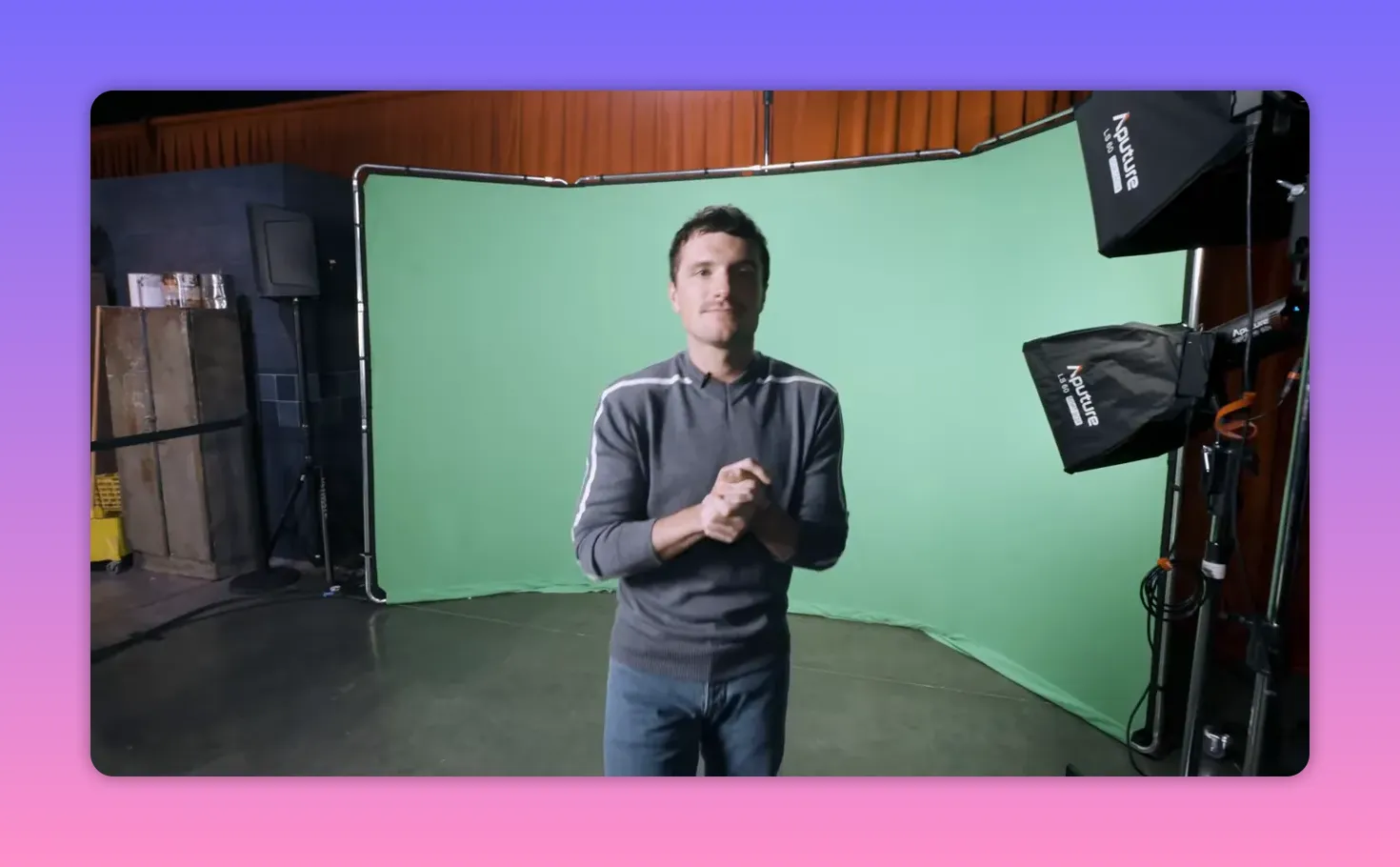 Actor standing centered in front of a green screen with studio lights and equipment visible.