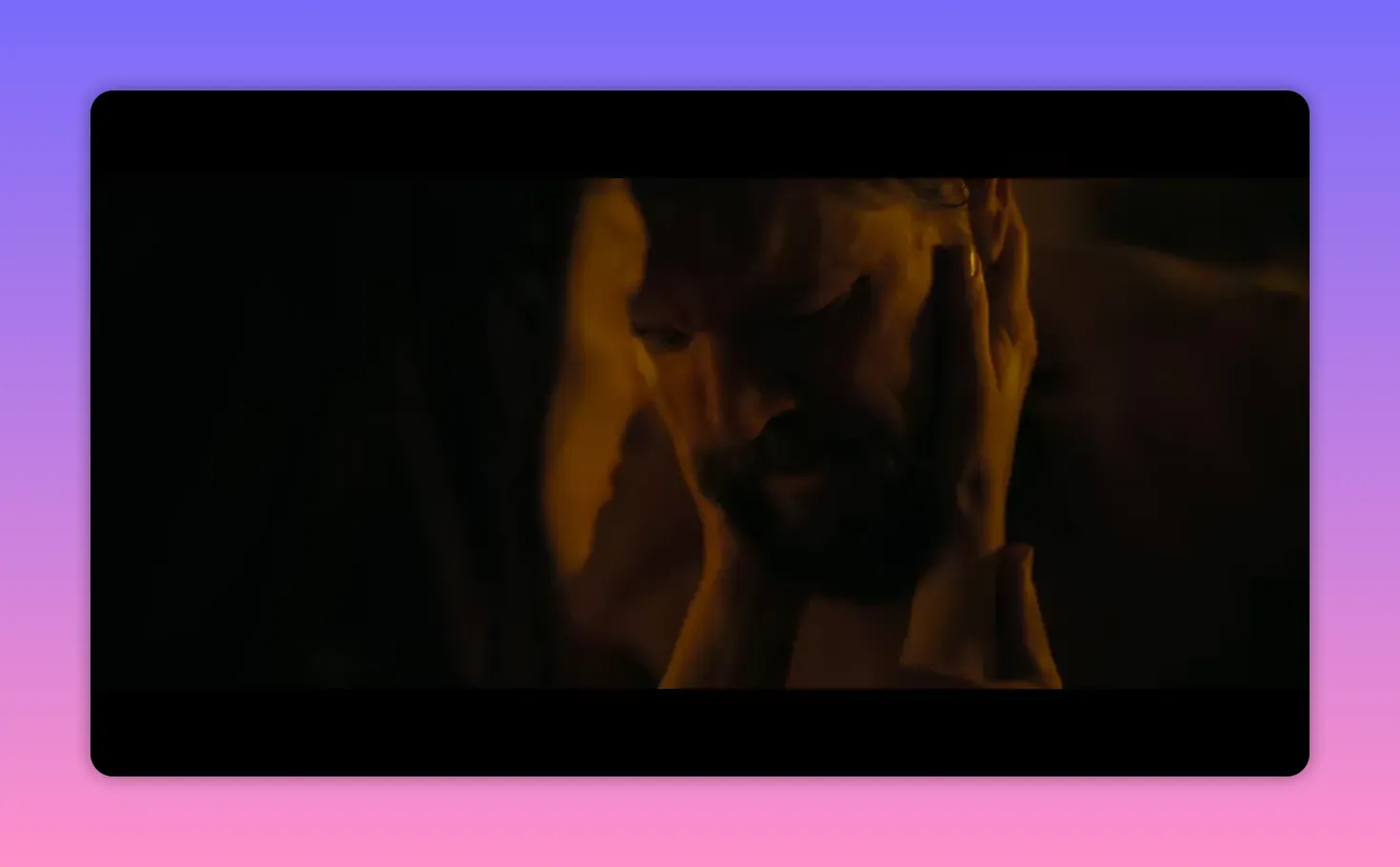 Dimly lit close-up of two people in an intimate moment, hands cradling a man's face