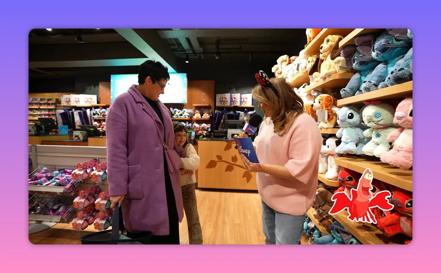 Host holding a Disney quiz card and microphone facing a participant in a Disney Store aisle, with plush toys clearly visible on shelves.