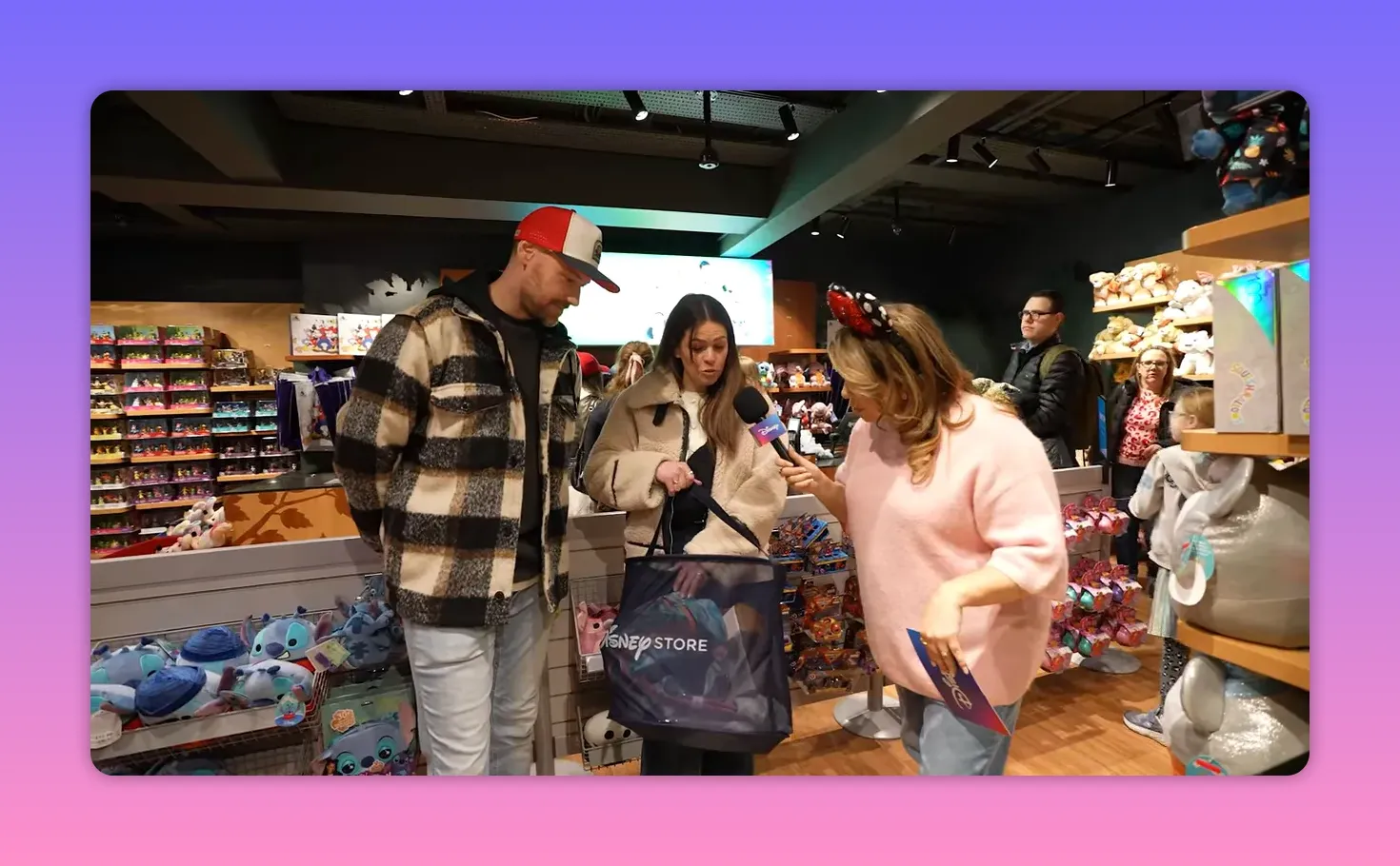 Presenter with microphone and card interviewing participants who hold a Disney Store prize bag in a crowded store