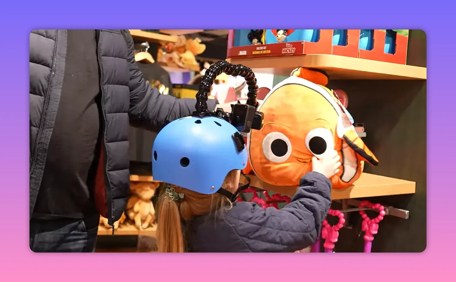 Child wearing a blue helmet fitted with a camera reaches to touch a Nemo plush on a Disney Store shelf