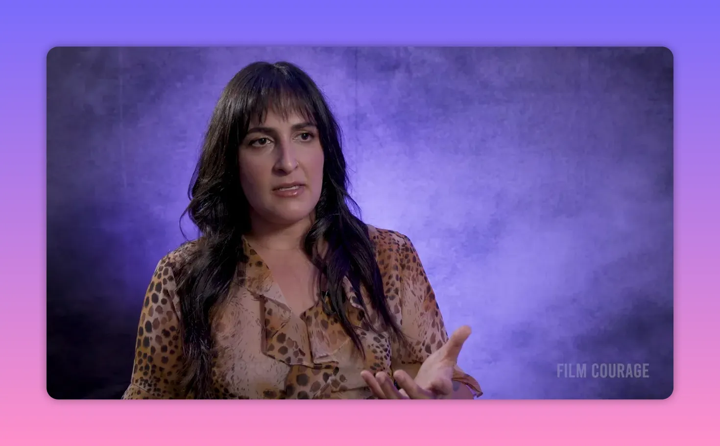 Interview subject speaking with open hands and a composed expression against a purple textured backdrop, sharp and well-framed.
