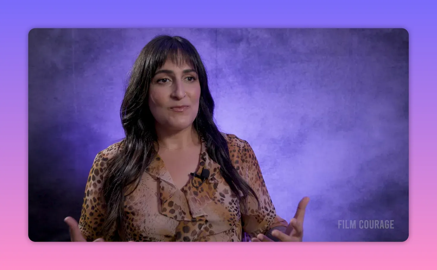 Interview subject gesturing with both hands while speaking against a textured purple backdrop, clear and well-lit.