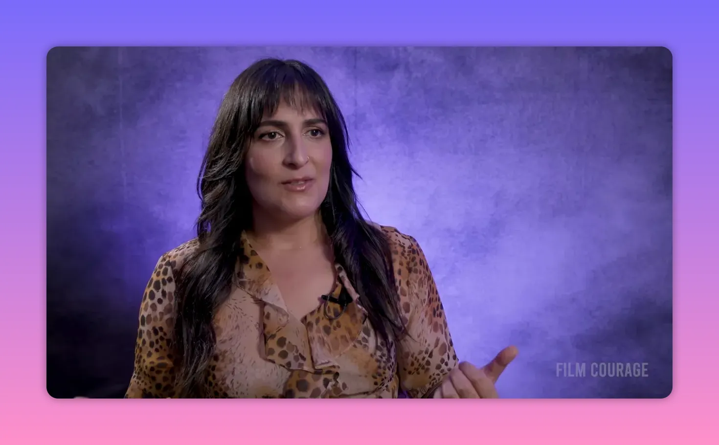 Interview speaker smiling slightly and gesturing with hands against a purple textured backdrop
