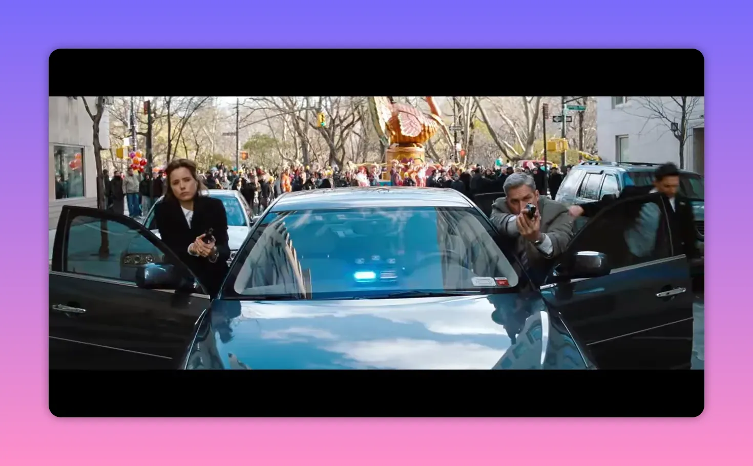 two officers drawing weapons beside a car with a large parade balloon and crowd in the background
