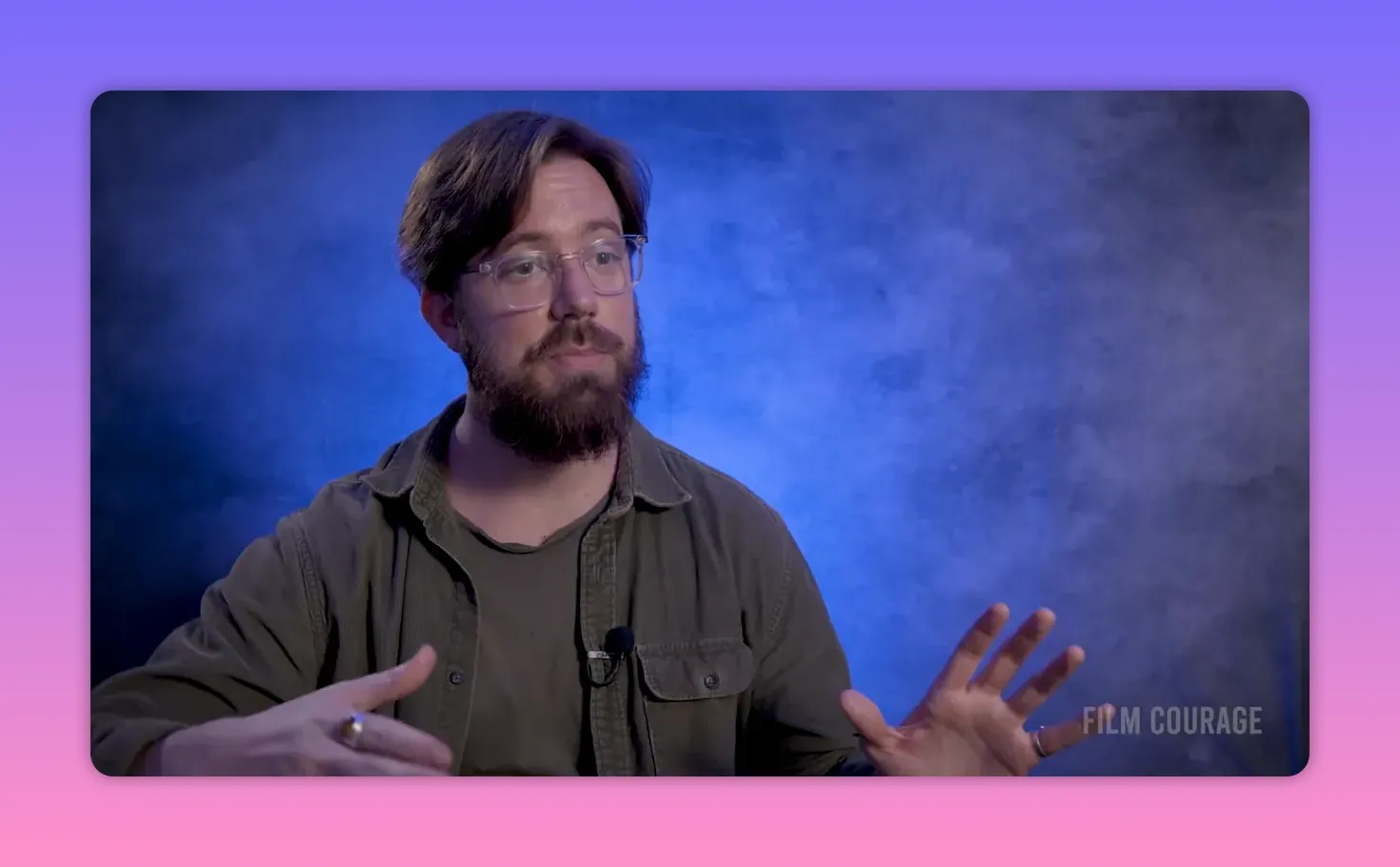 Filmmaker speaking clearly against a blue textured backdrop, hands framing the idea while discussing distribution and release.