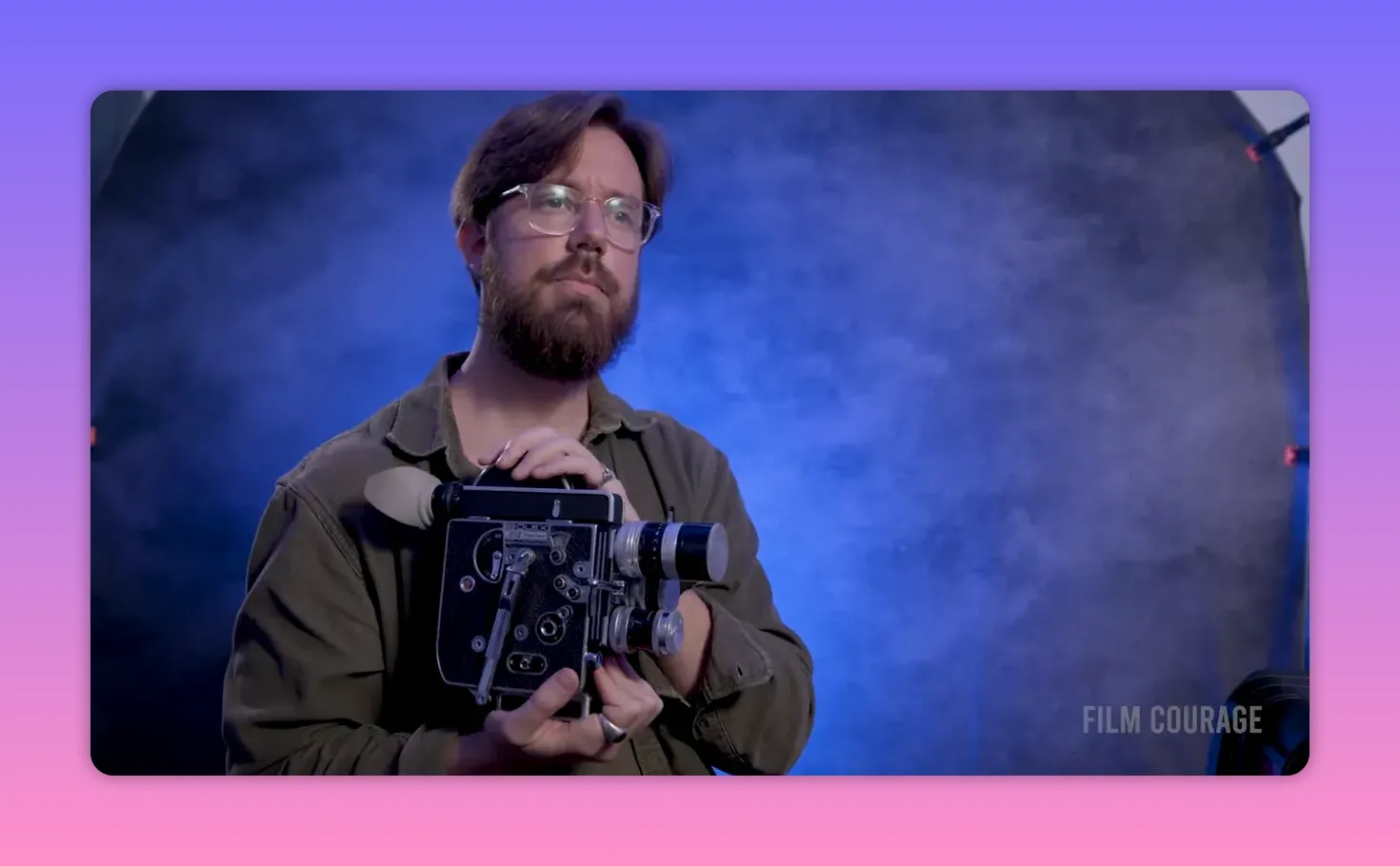 Mid-shot of a person holding a Bolex 16mm film camera with a blue textured backdrop and studio grip visible.