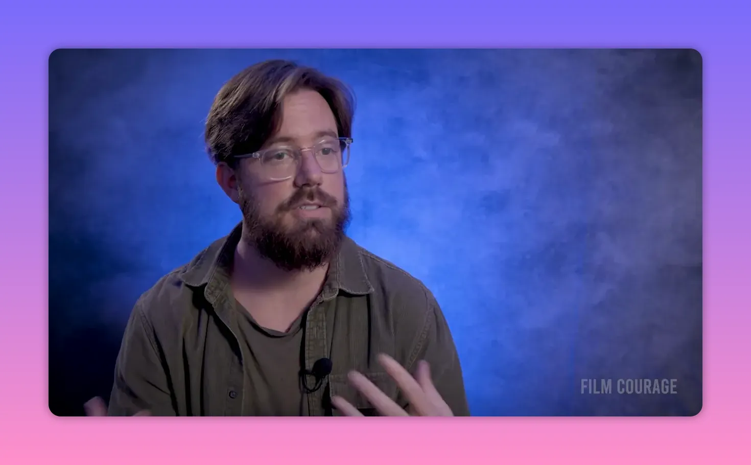 Filmmaker mid-interview with hands gesturing against a blue textured backdrop, mid-shot.