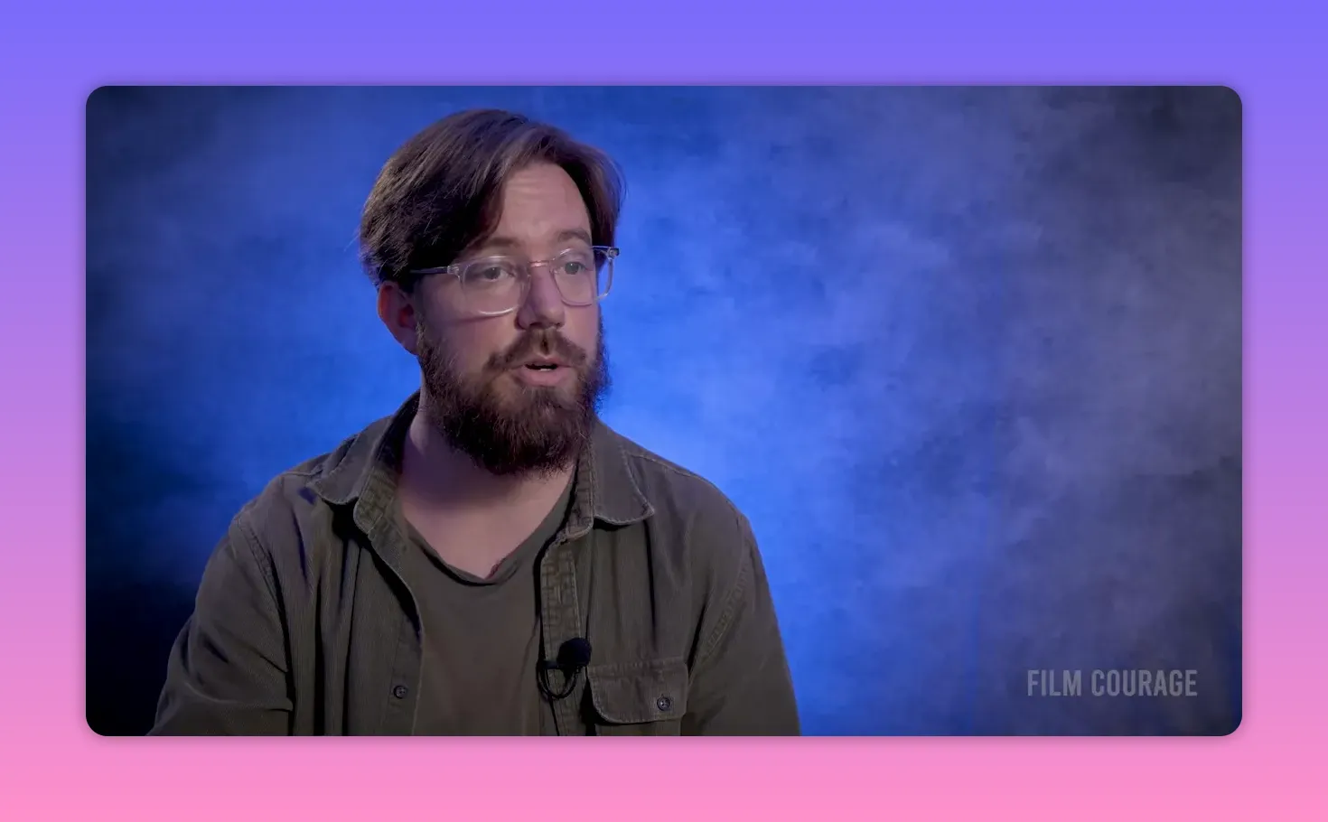 Filmmaker in a medium shot against a blue textured backdrop, looking thoughtful and speaking gently, microphone visible on his shirt.
