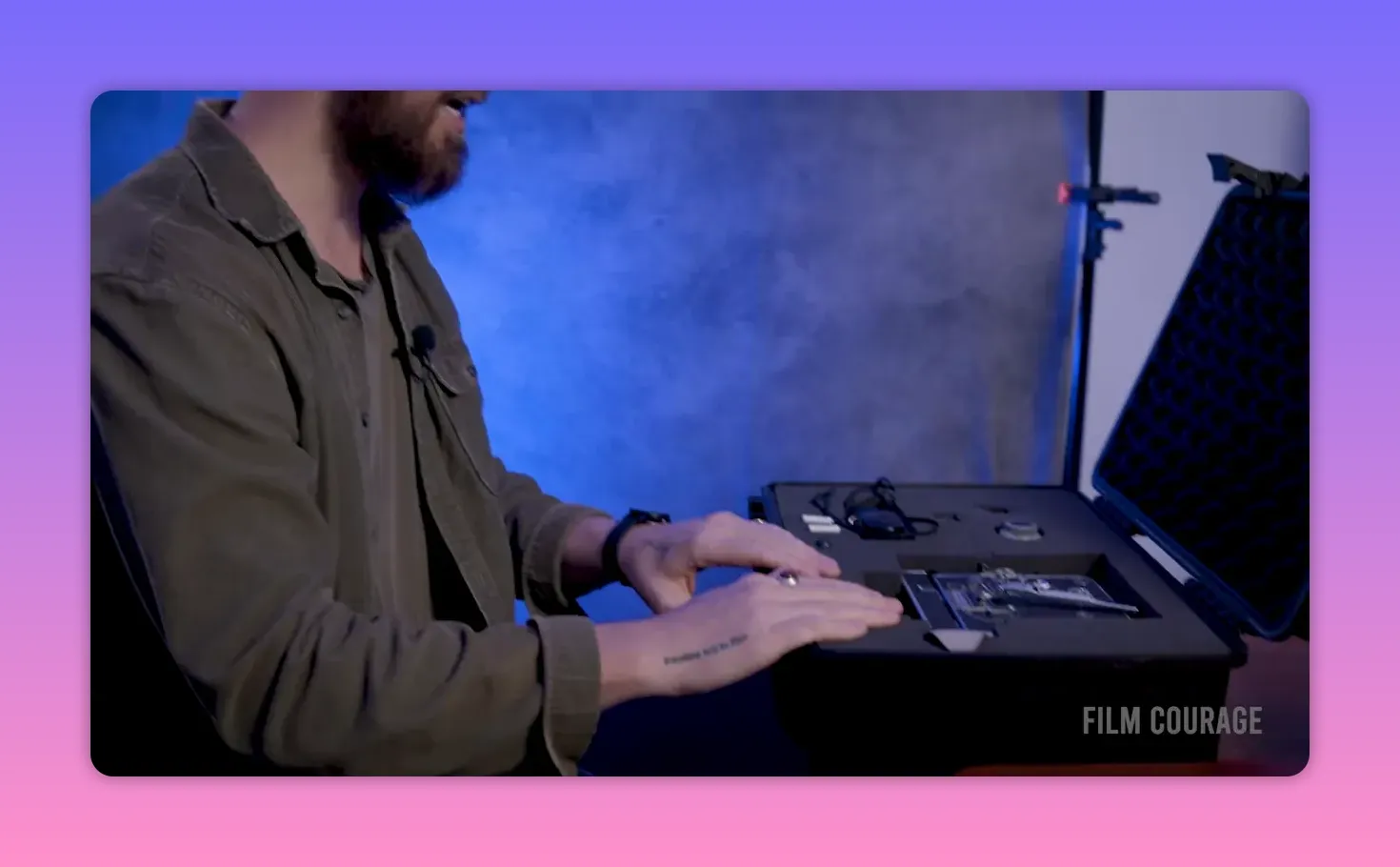 Close view of hands resting on an open foam-lined case with camera components visible, the filmmaker speaking off-frame, blue textured background.