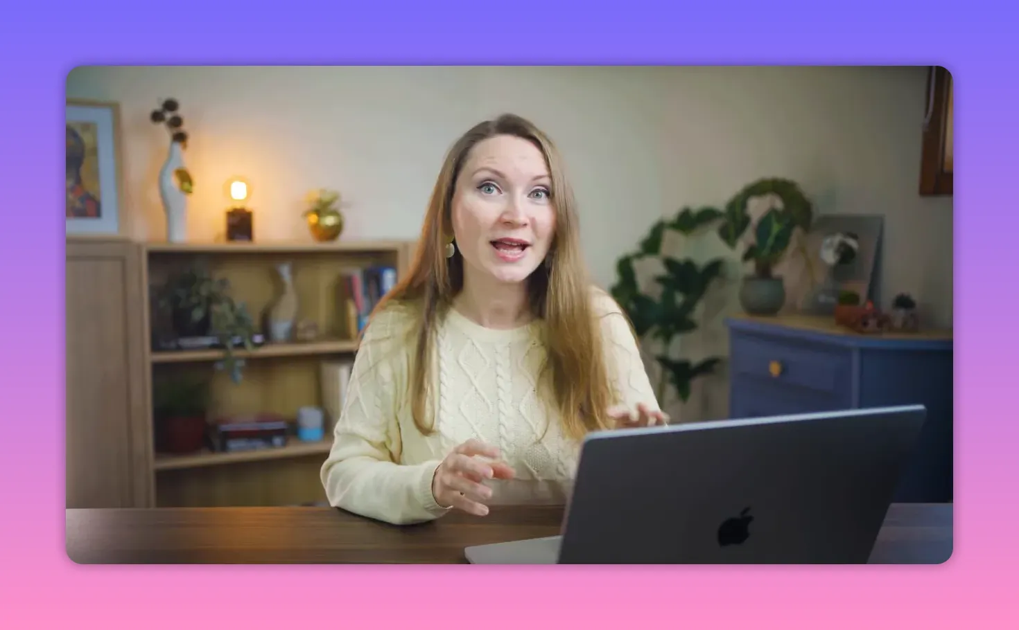 creator smiling and gesturing while working on a laptop at a desk with shelf in background