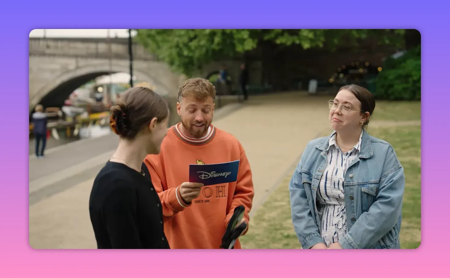 Host holding a blindfold and reading a Disney prompt to two contestants before the blindfolded mimic challenge.