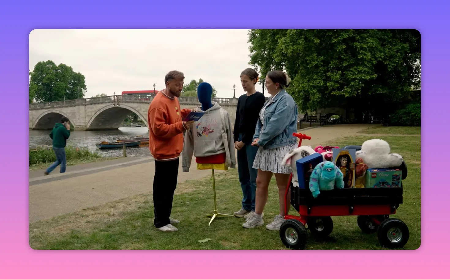 Wide shot of the host, a mannequin wearing clothes, two contestants and a wagon of prizes preparing for the clothes-on-mannequin challenge