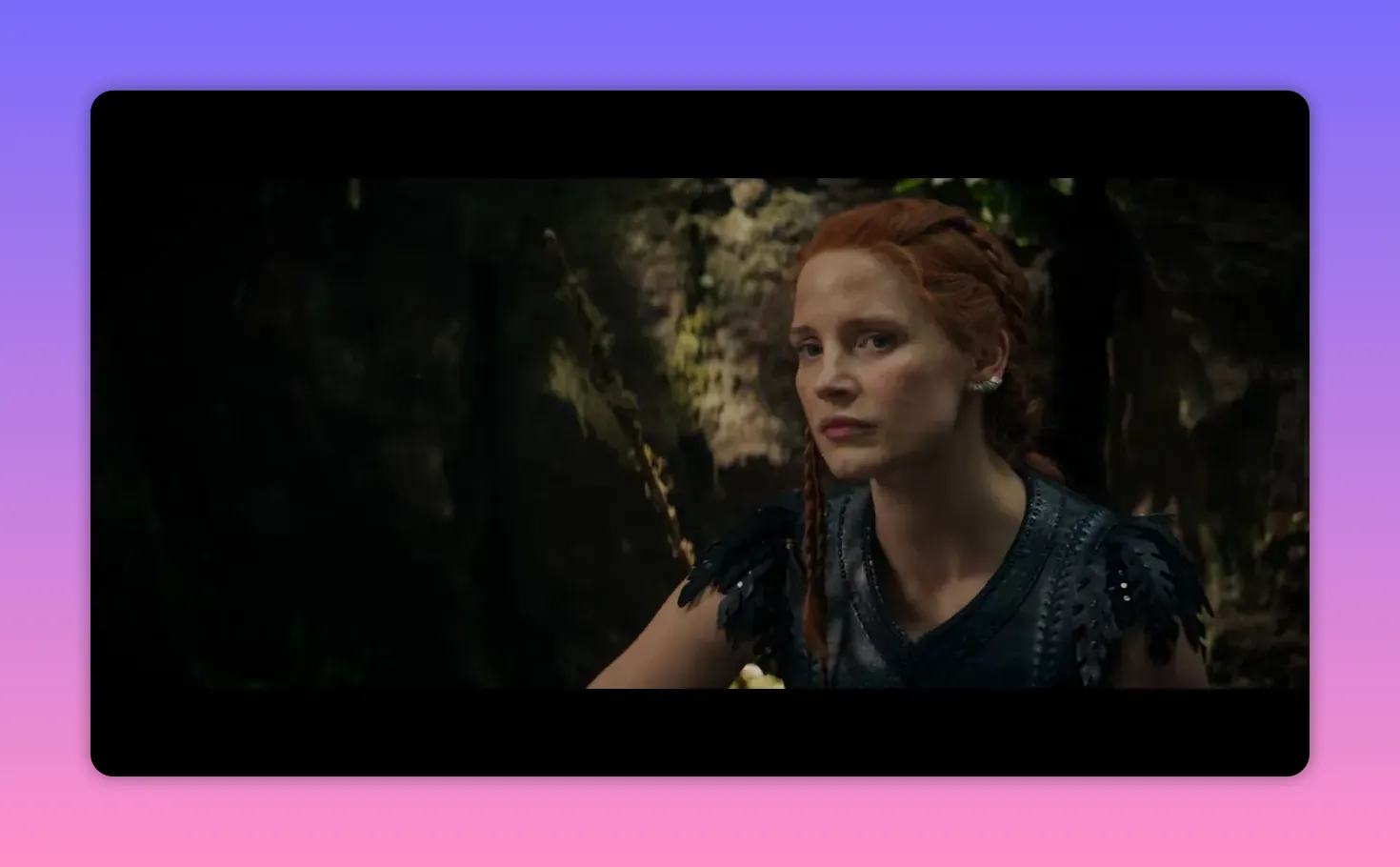 Frontal three-quarter shot of a red-haired woman glancing toward the camera in the woods, alert and composed.