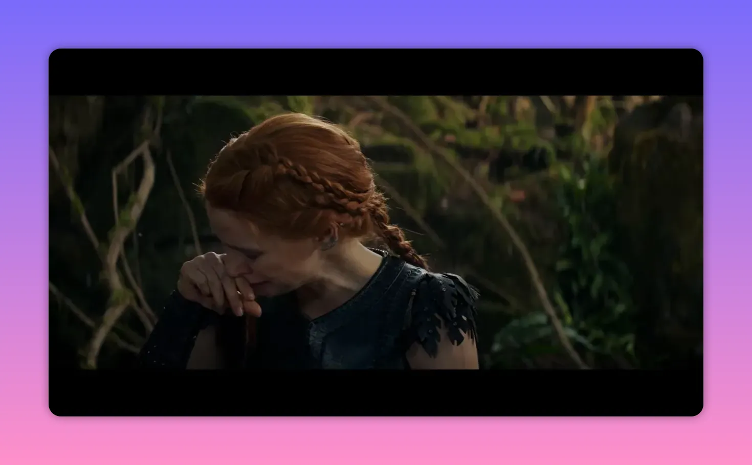 Red‑haired woman stifling emotion with her hand, eyes downcast in a mossy forest clearing.