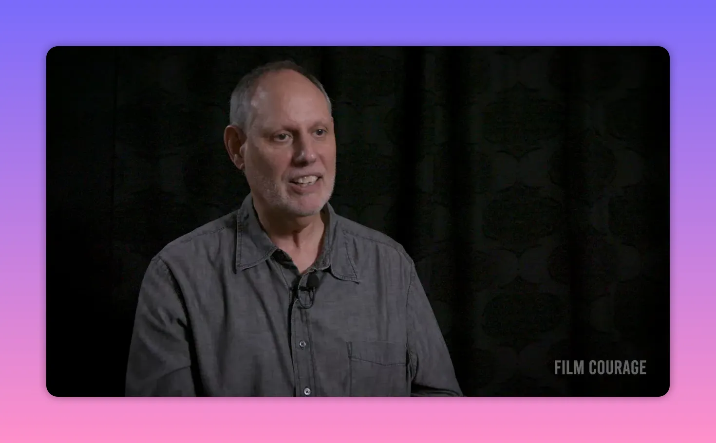 Composed mid-shot interview subject smiling and reflecting about storytelling against a dark backdrop
