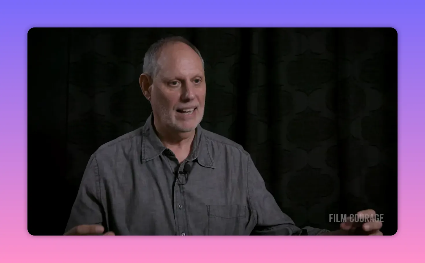 Interviewee gesturing with hands while speaking against a dark curtain backdrop.