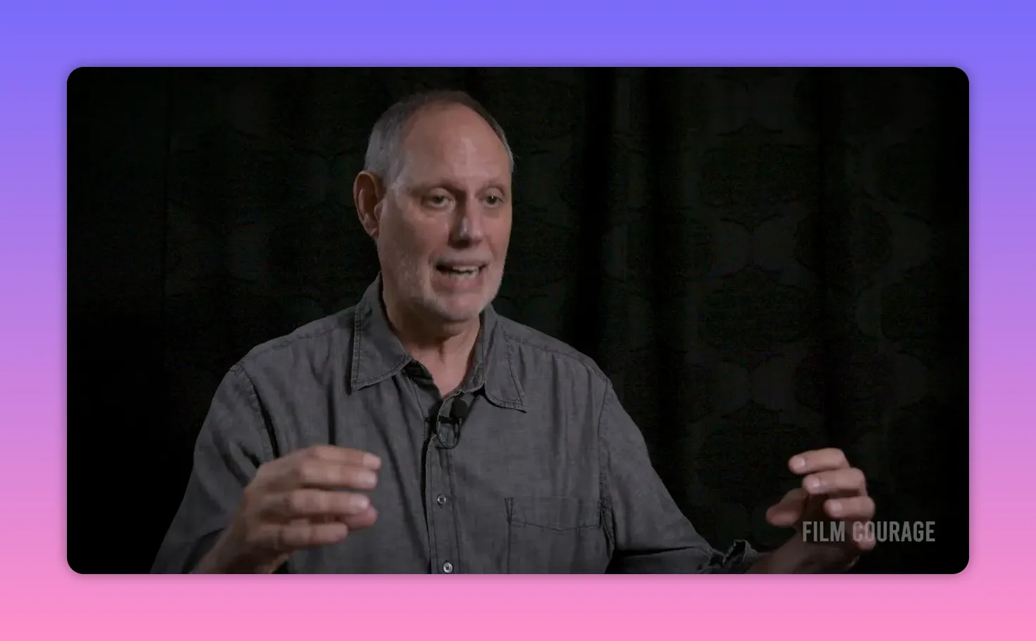 Interview subject gesturing with both hands while explaining narrative framing, dark background