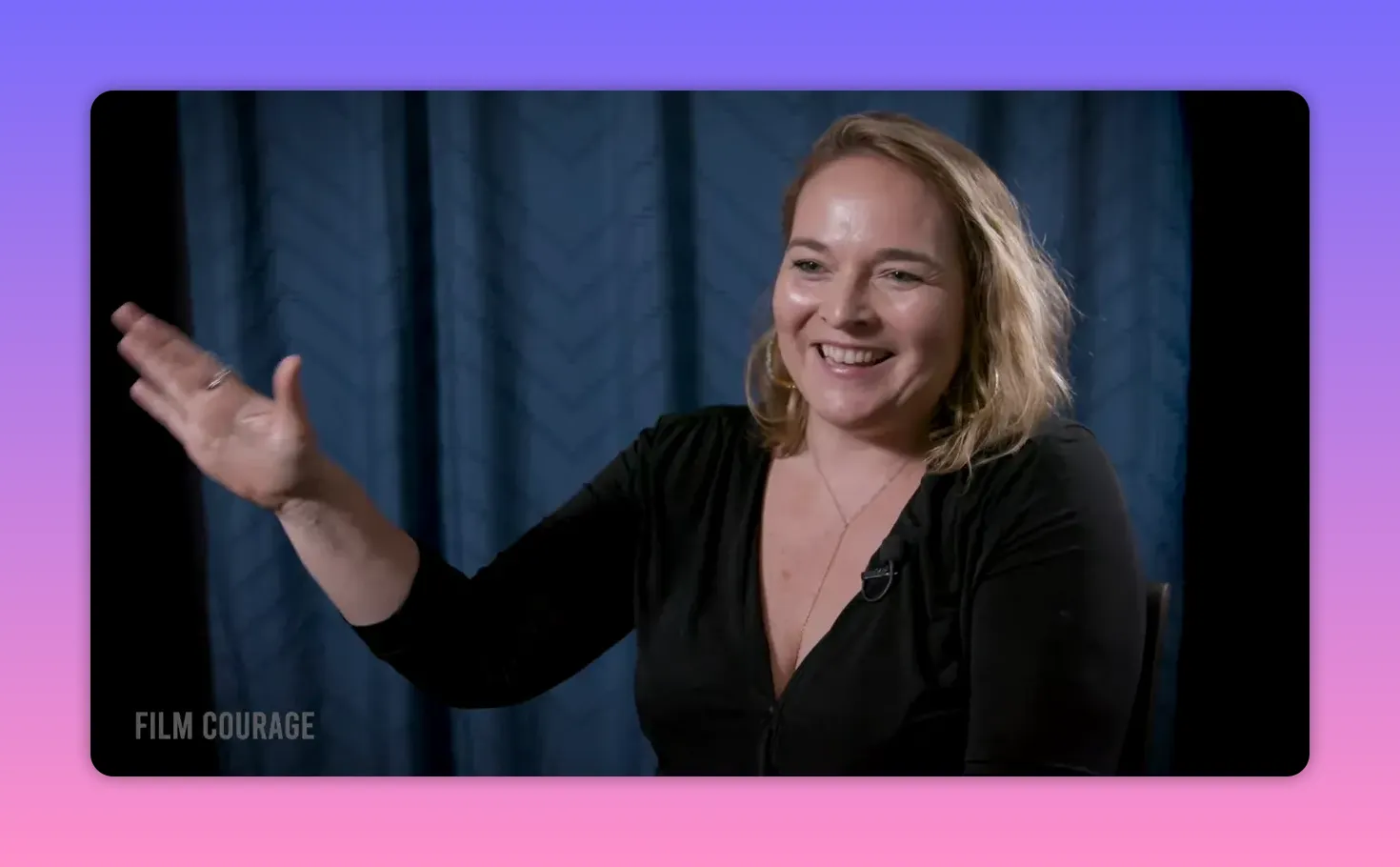 Three-quarter interview shot of a filmmaker smiling and gesturing openly, clear lighting with blue curtain background.