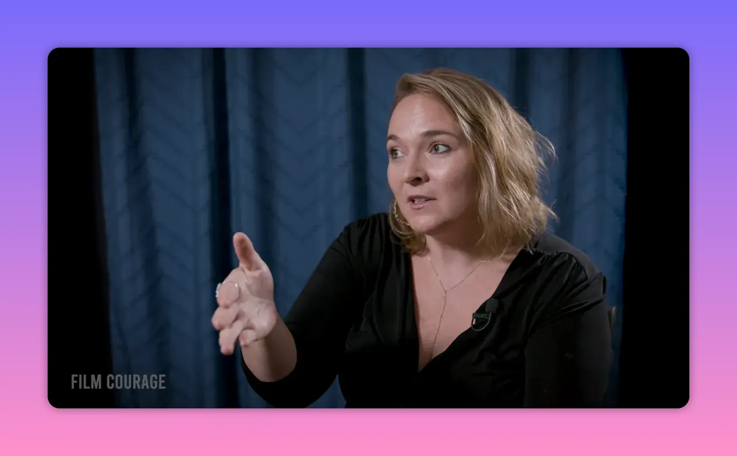 Interview subject extending hand forward in an explanatory gesture against a blue curtain backdrop, Film Courage watermark.