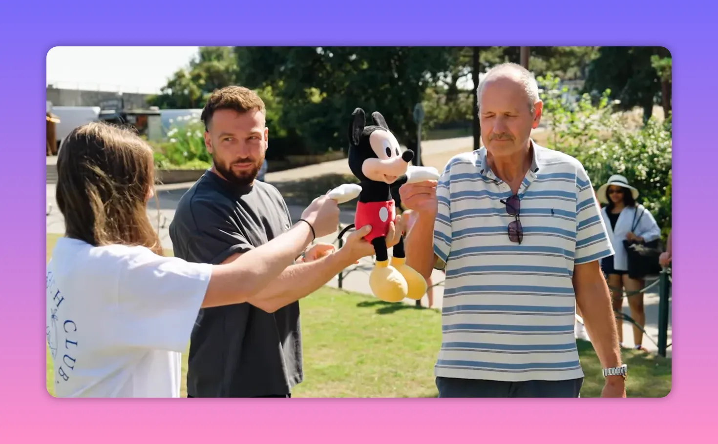 Wide shot of granddaughter, host and grandfather each holding one of Mickey Mouse plush&rsquo;s hands in a park