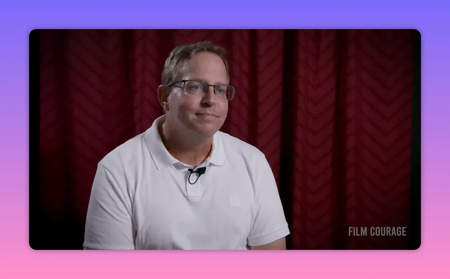 Clear mid-shot of interview subject in white polo looking engaged with a lapel mic and patterned maroon curtain backdrop, Film Courage watermark