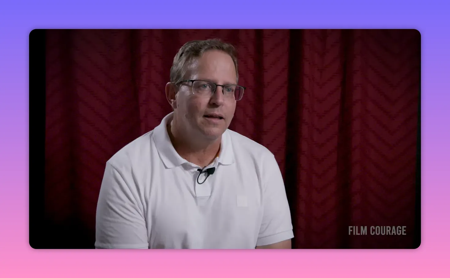 Clear mid-shot of interview subject in white polo speaking with an engaged expression against a maroon curtain, lapel mic visible, Film Courage watermark