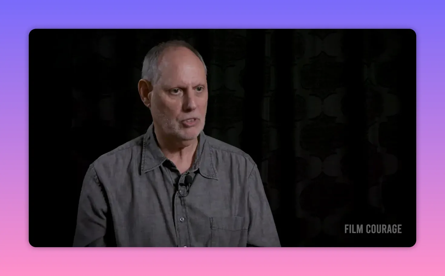 interviewee speaking in a gray shirt against a dark backdrop with a steady, reflective expression
