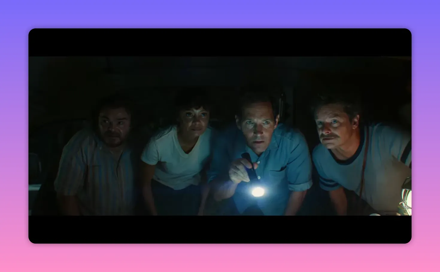 Four people huddled together in the dark, one holding a flashlight