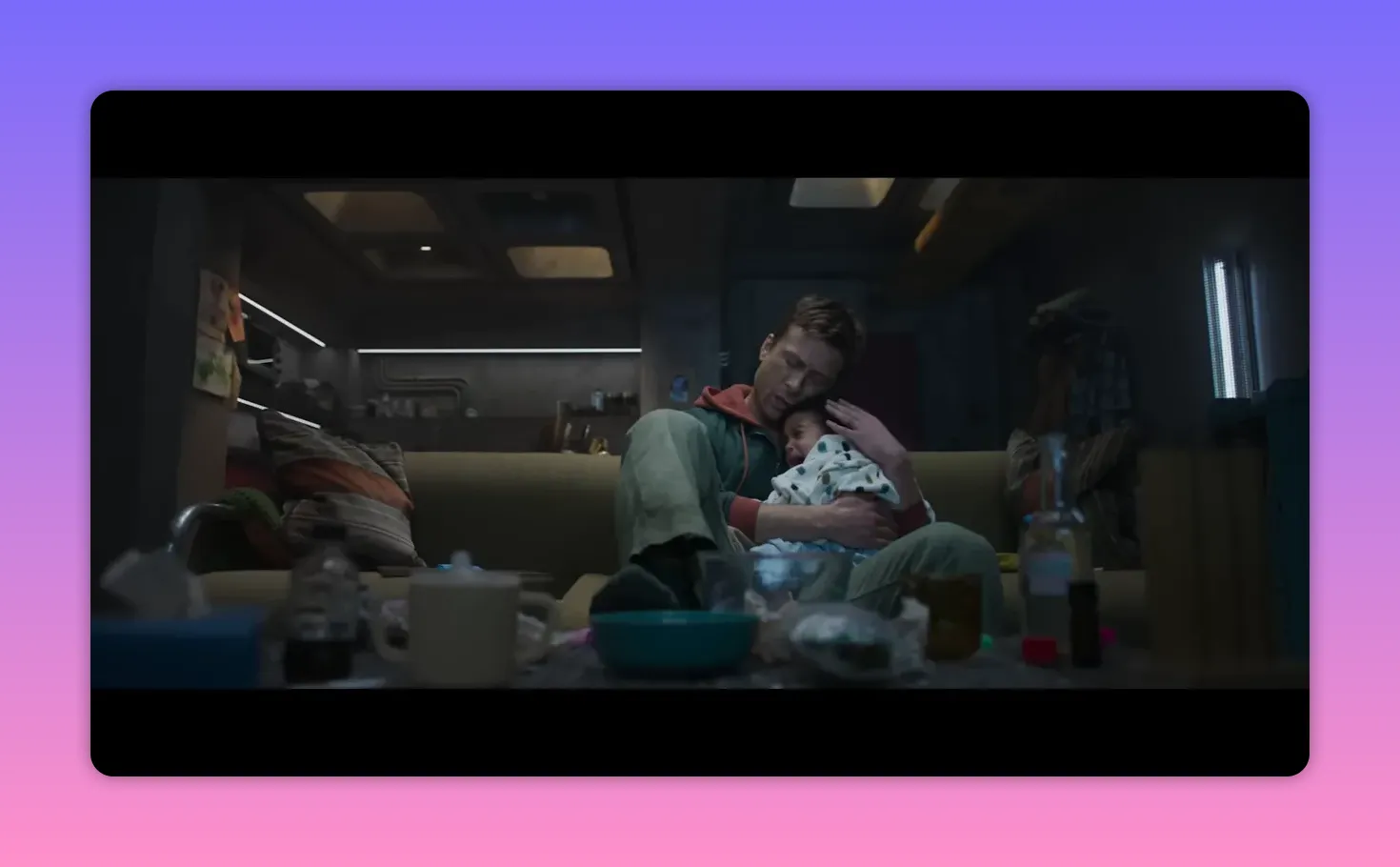 Wide shot of a man sitting on a messy couch, holding a young child tightly in a dim living room.