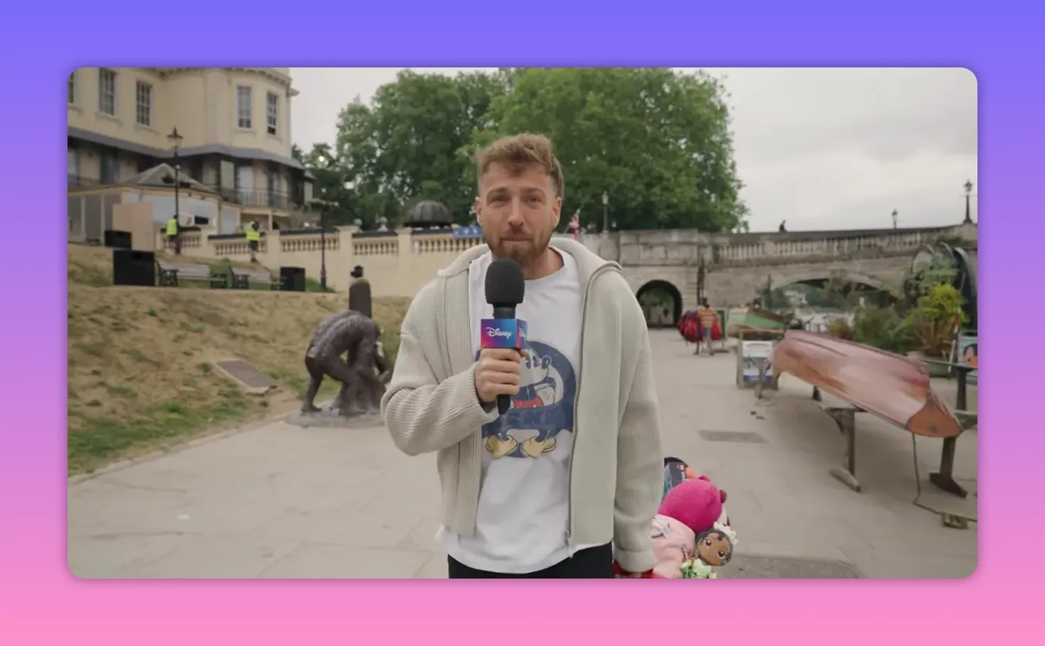 Sam Thompson holding a Disney-branded microphone on the Richmond upon Thames riverside with prizes visible behind him.