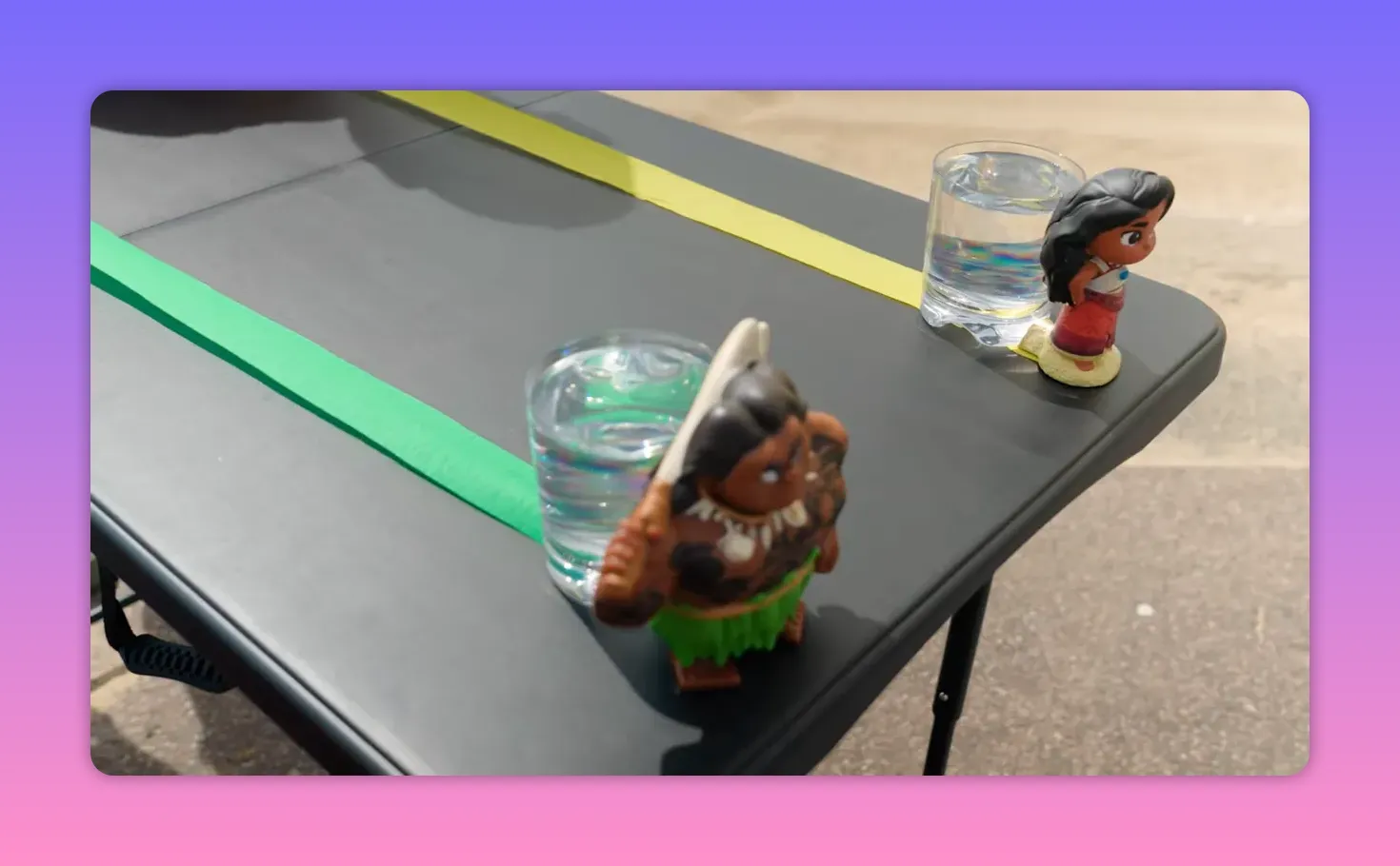 Close-up of two character toys beside clear cups of water on a table with colored rolling tracks